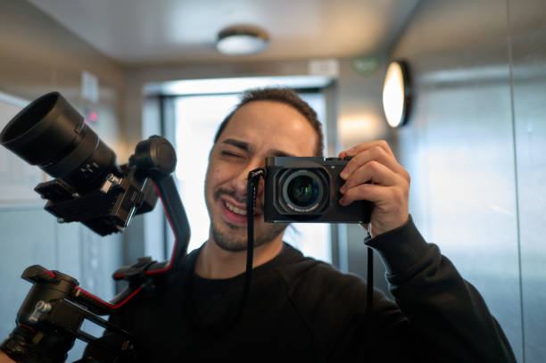 Videographer taking a selfie with a mirror in an elevator while holding a gimbal and a camera