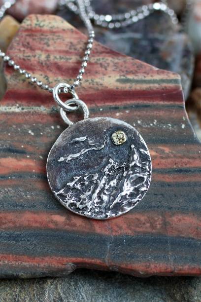 istock Artistically crafted silver mountain pendant with yellow gold moon on a textured stone background. 2197377708