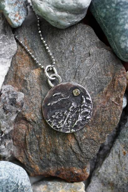 istock Handmade silver pendant with a mountain range and a moon on a silver chain on a textured stones. 2197377733