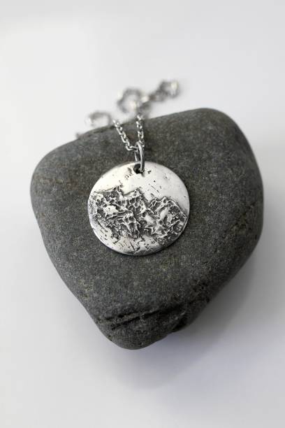 istock Handmade round silver pendant with a unique and textured surface on a rock and white background. 2197378842