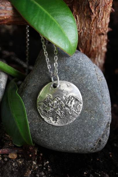istock Silver chain with handmade pendant with a mountain range design on stone with tree and leaves. 2197378917