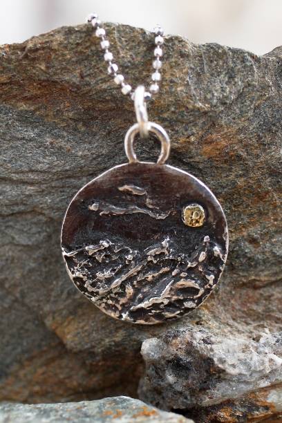 istock Handmade silver pendant with a rough mountains texture and a small gold moon on a silver chain. 2197379074