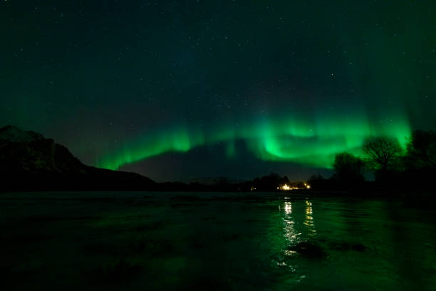 Northern Lights, polar light or Aurora Borealis in the night sky over the Vesteralen islands in Northern Norway. Panoramic image with snow covered mountains and a lake in the foreground.