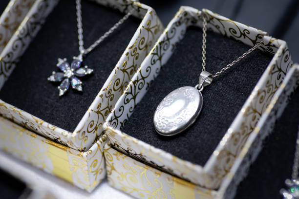 A beautifully crafted silver oval locket pendant necklace with engraved patterns, displayed in an elegant jewelry box