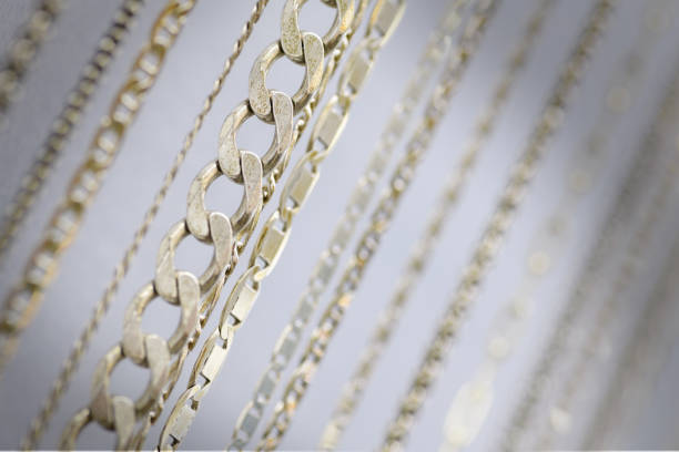 Close-up of various silver chain necklaces hanging on a display stand, showcasing different chain styles