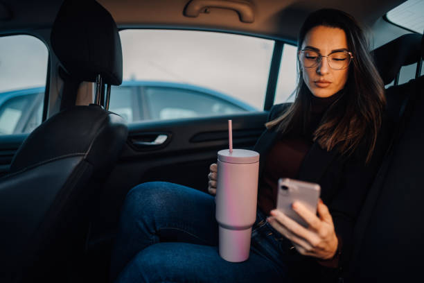 istock Businesswoman using smartphone and drinking beverage in car back seat 2197384713