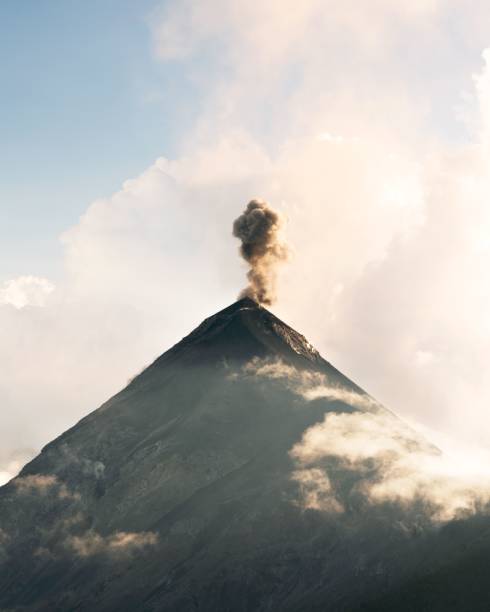 istock A majestic volcano emitting smoke under a clear sky, surrounded by clouds. 2197386570