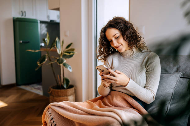 istock Young woman using smart phone while relaxing on a sofa wrapped in blanket 2197391188