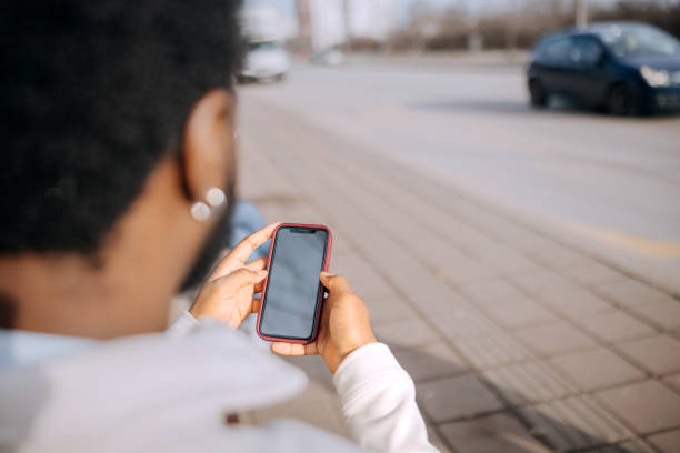 istock Over the shoulder view of young man using smart phone with blank screen while sitting on bus station 2197392411