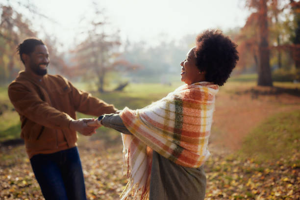 Happy African American couple having fun while holding hands and spinning during autumn day in the park. Focus is on woman.