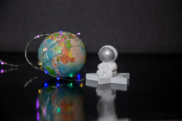 istock Mini astronaut sitting on a star beside a globe wrapped in fairy lights 2197393851
