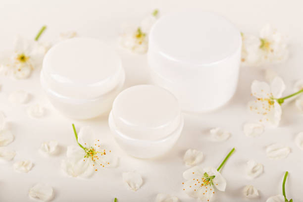 Mockup. Set of white cosmetic containers surrounded by white spring flowers. Concept beauty, skincare or natural product. Cosmetic jars and containers for cream or cosmetic products