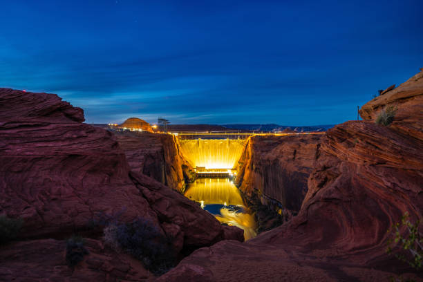 Night view of Glen Canyon Dam in Arizona, illuminated against the red rock canyons. This stunning scene captures the engineering marvel of the Colorado River hydroelectric dam, blending technology with the beauty of the Southwest.