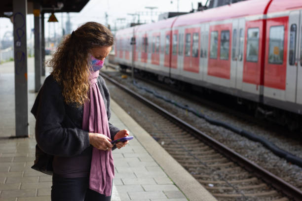 istock Woman with face mask waiting at platform looking at cellphone 2197403942