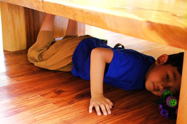 istock A young boy plays joyfully under a wooden table with a small toy car. 2197418580