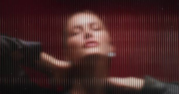 A woman looks at the camera standing behind a striped glass. She's posing in the studio. Close-up of her face