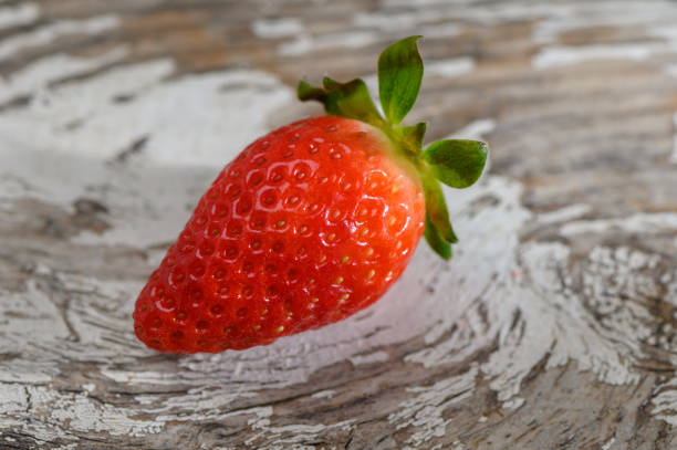Brightly colored strawberry with vibrant seeds showcases summer's bounty on a distressed wooden table.