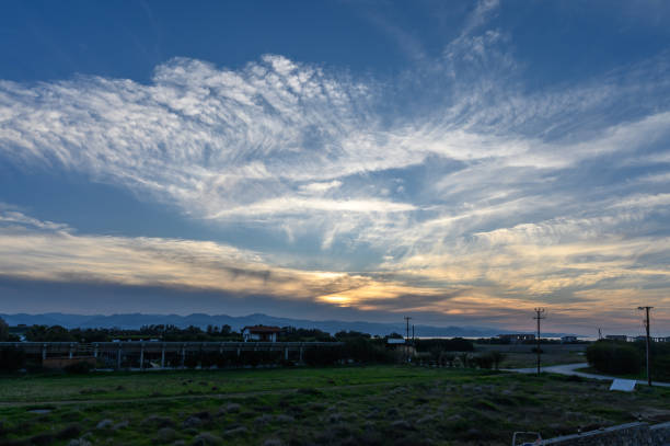 Dramatic sunset paints the sky in hues of gold and blue over quiet fields and distant mountains
