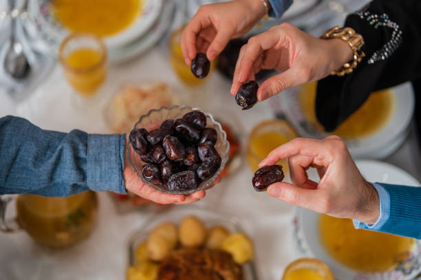istock Happy Muslim family having iftar dinner to break fasting during Ramadan dining table at home group of Islamic people eating a healthy food dates together sharing and giving. 2197423445