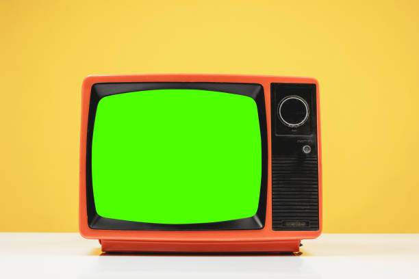 Old retro red TV with chroma key green screen on white table with on yellow background, front view.