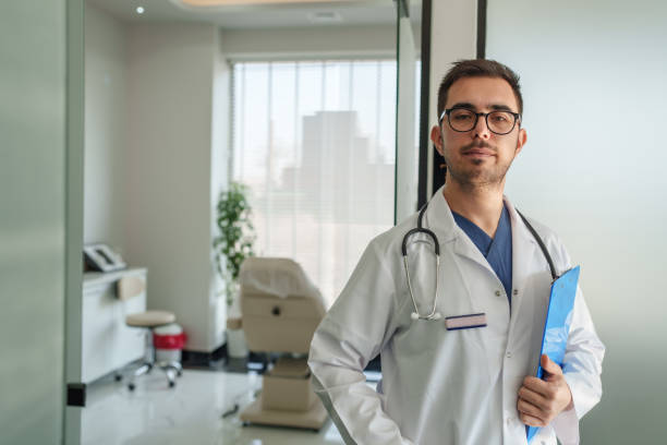 istock Doctor with white coat, looking at camera in front of his office. 2197428914