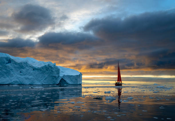 istock red sailboat sailing among floating icebergs in Disko Bay glacier with orange sunset during polar summer midnight solar season. Ilulissat, Greenland 2197431797