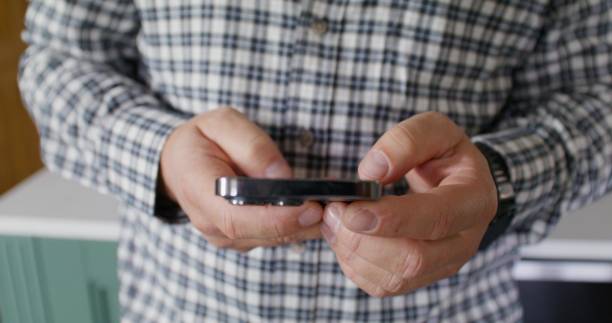 Close-up of man's hands with a mobile phone. He's typing. Unrecognizable person, home interior