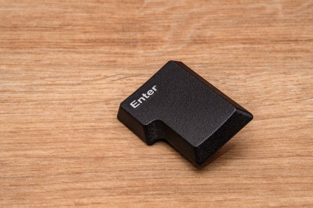 Enter key. Detached Enter key from a keyboard, placed on a wooden surface. The key is showing its textured surface and distinctive L-shape.