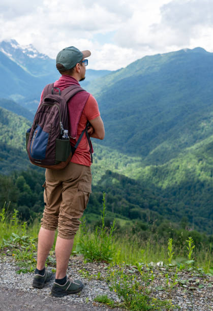 istock man traveler with backpack looking breathtaking mountain landscape Wearing green cap , red shirt, looks over green hills , peaks under cloudy sky. outdoor adventure, beauty of nature Hiking 2197441447