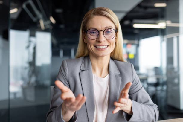 istock Businesswoman smiling and gesturing talking looking at camera, woman working in office using laptop for online video call, remote conference meeting 2197444712