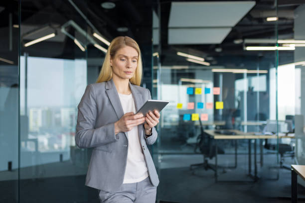 istock Serious concentrated woman standing by the window inside the office with a tablet computer, businesswoman reviewing electronic financial report, thinking and focused 2197444769