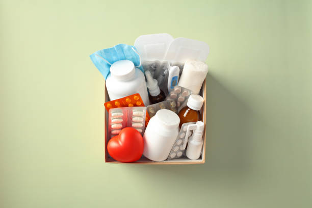 istock Medical supplies box with various items including pills, bottles, a heart-shaped object, a thermometer, bandages, and a face mask on a light green background. Medical donation box concept 2197463410