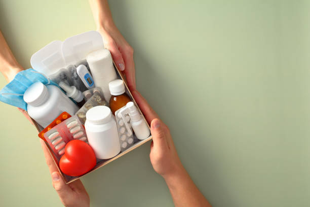 istock Hands holding a first aid kit containing various medical supplies, including pills, a thermometer, bandages, and a face mask, against a green background 2197463441