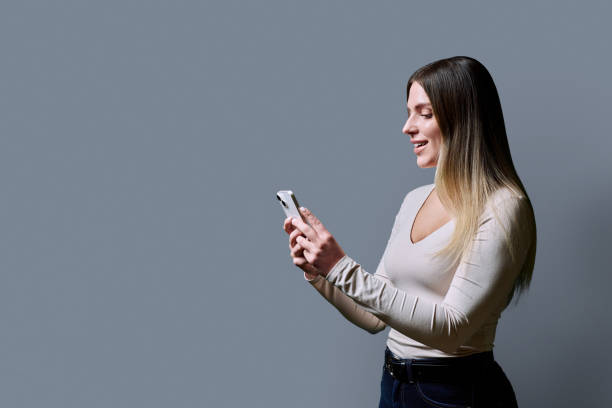 istock Profile view, young beautiful woman using mobile phone on grey background 2197464961