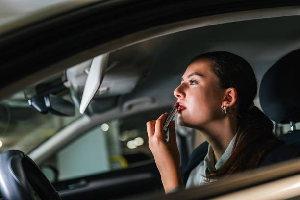 istock Young woman putting a red lipstick while sitting in a car. 2197466184