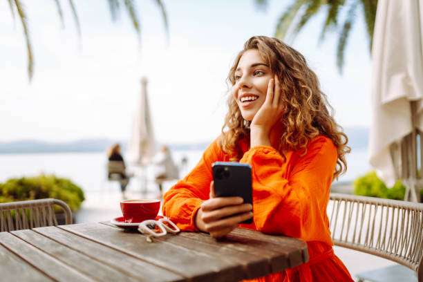 istock Happy beautiful woman using mobile phone while drinking coffee in cafe outdoor. 2197466490