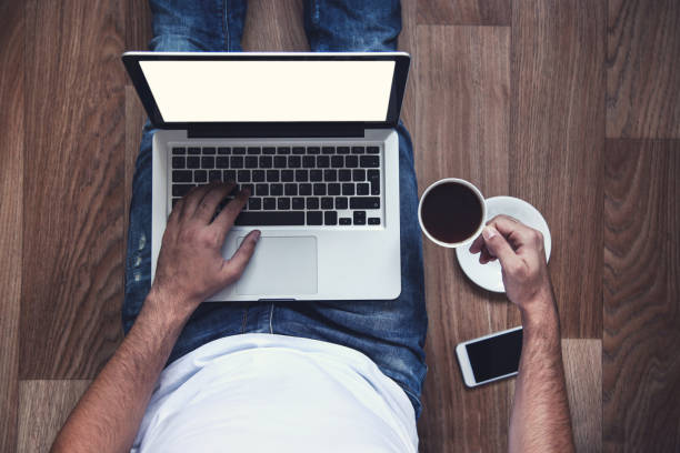 istock Man sitting on the floor using laptop computer with cup of coffee and smartphone 2197467328