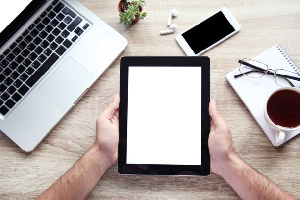 Male hands holding tablet computer with laptop, smartphone and cup of tea on table