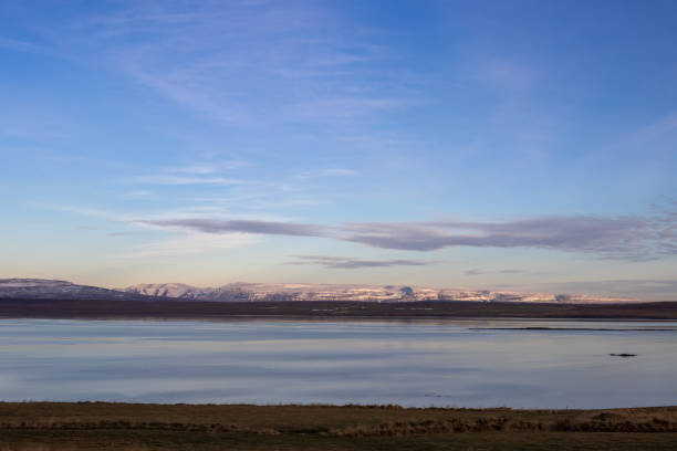 View from an autumn meadow on a calm water of a fjord of Atlantic ocean. Mountains with snow on a horizon. Blue sky with light clouds. North of Iceland.
