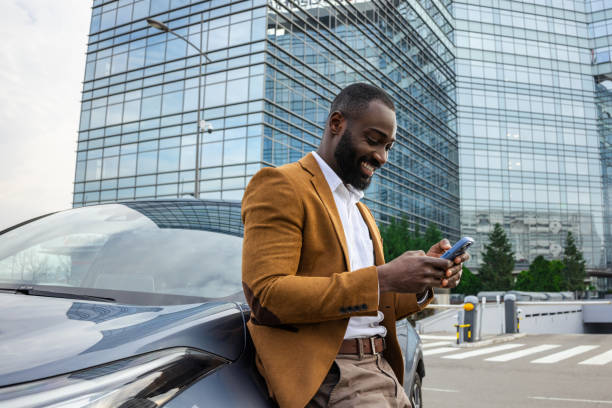 istock Smiling professional man checking smartphone while leaning on his car 2197480895