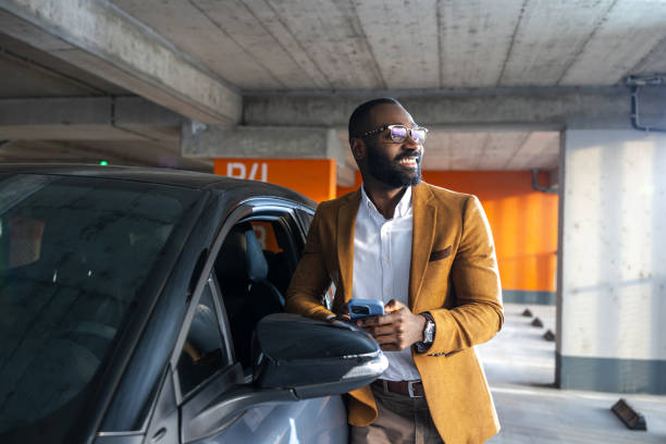 istock Man smiling near car in parking garage using smartphone for casual browsing 2197481330
