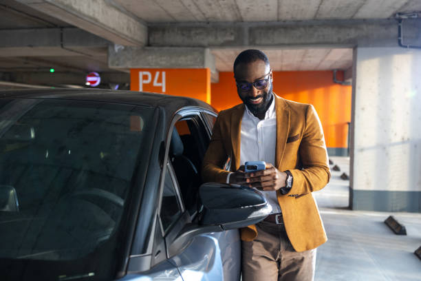 istock Man smiling near car in parking garage using smartphone for casual browsing 2197481331