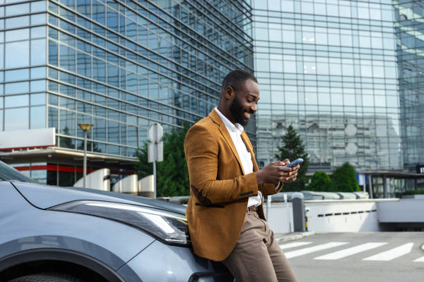 istock Man leaning on car with smartphone near modern office building 2197481531