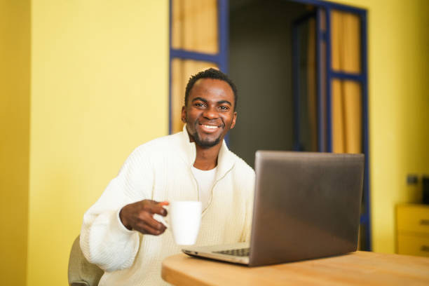 istock Young african american man working on laptop in cafe drinking coffee on break 2197483394