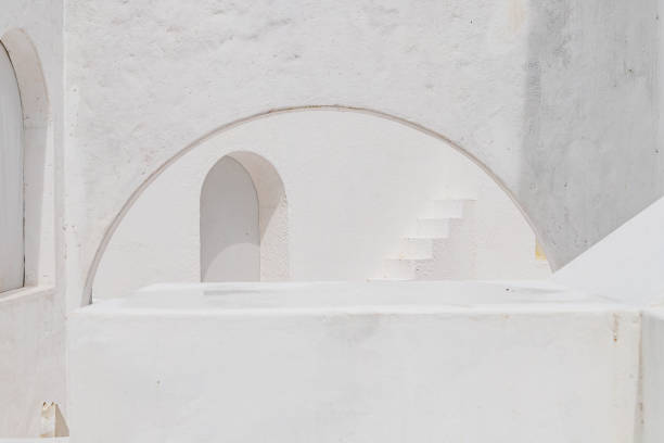 curved and arched white textured walls frame a staircase in a sunlit architectural scene.