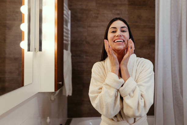 istock Young woman applying face cream and smiling in bathroom 2197491850