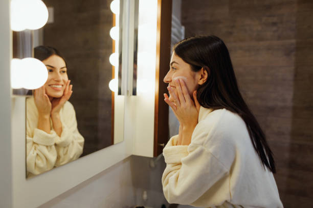 istock Young woman applying moisturizing cream on face in bathroom 2197491864