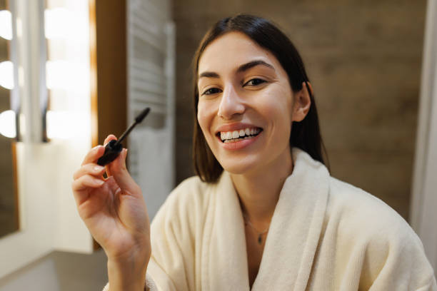 istock Smiling woman applying mascara in bathroom mirror getting ready 2197491915