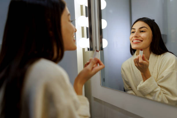 istock Young woman applying lipstick in bathroom mirror with led lights 2197491932