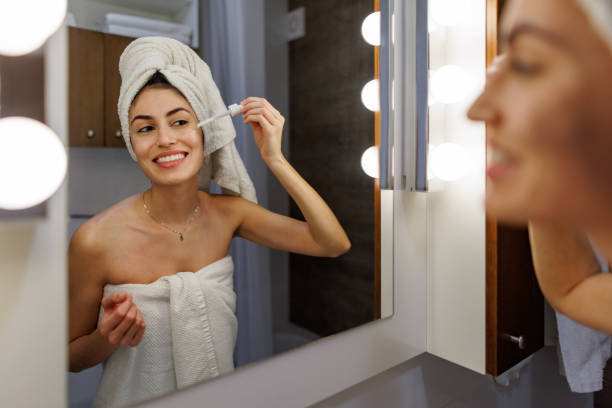 istock Young woman applying serum on face in bathroom mirror 2197492057